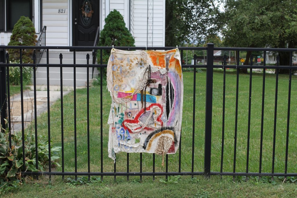 Image: Peoria Guild of Black Artists, Banner at 821 N. 5th Street, Springfield IL. A vertical banner containing various colors and shapes hangs on a black fence in front of a white house. Photo by Jeff Robinson.