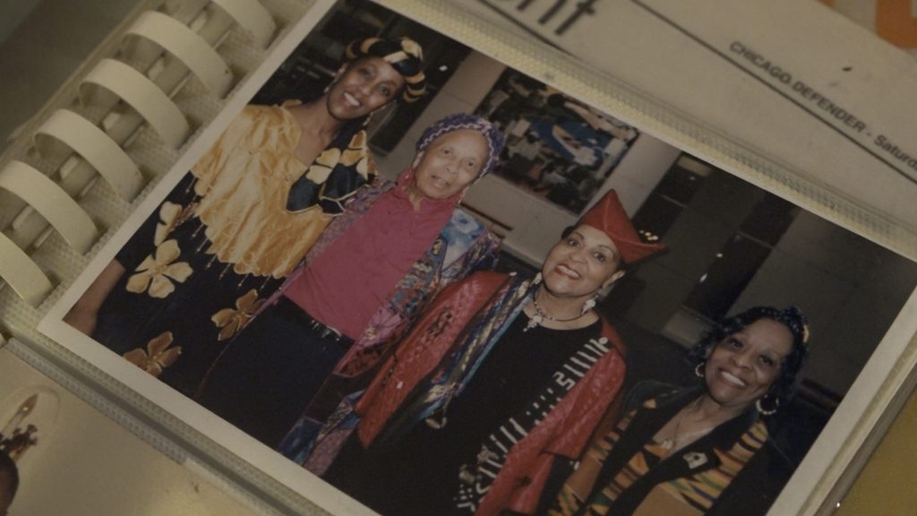 Image: Blackburn is posed in black and gold at the left of this image beside her lifelong mentor, Margaret Burroughs in purple and pink. The photo includes Val Gray Ward in the red hat, and ETA Arts Foundation director Abena Brown at the far right. (1990s). Photo of image by Wills Glasspiegel.