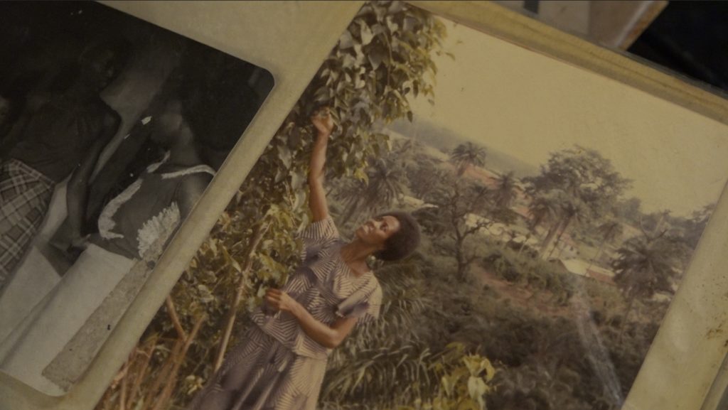 Image: Darlene Blackburn in Nigeria, 1980. She is smiling while reaching up into a tree. Photo of image by Wills Glasspiegel.