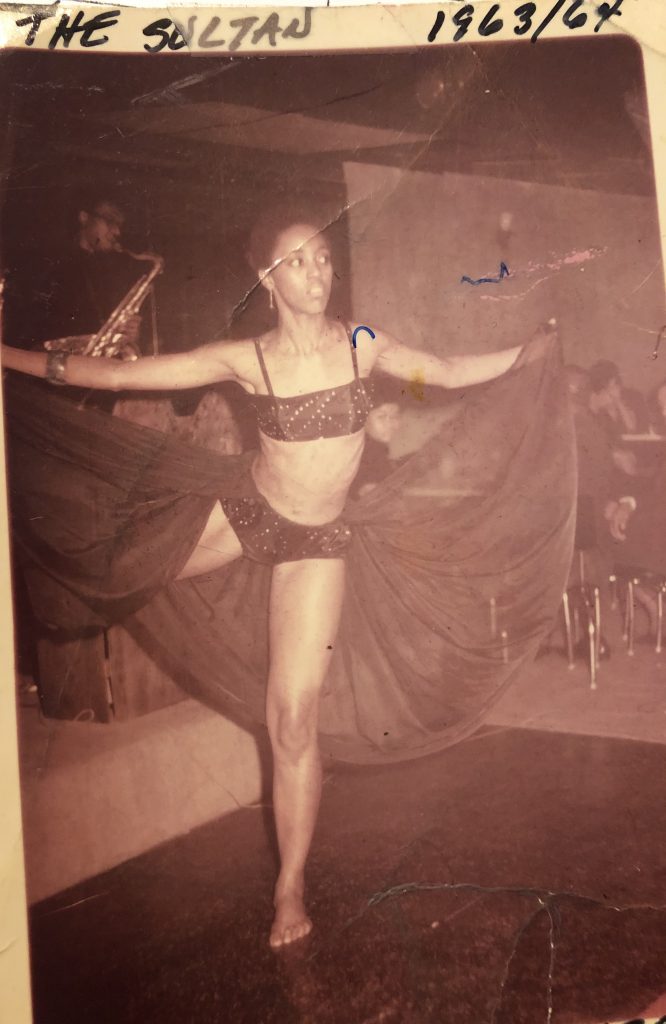 Image: A photo of Darlene Blackburn dancing on one leg with her skirt up in her hands. “I used to call it ‘dancing on a time,’ Blackburn says. “I’d say to my dancers, ‘if you can dance in a small place, then you know you can dance in a big place.’ Behind me on the saxophone is Eugene Easton.” Photo of image by Wills Glasspiegel.