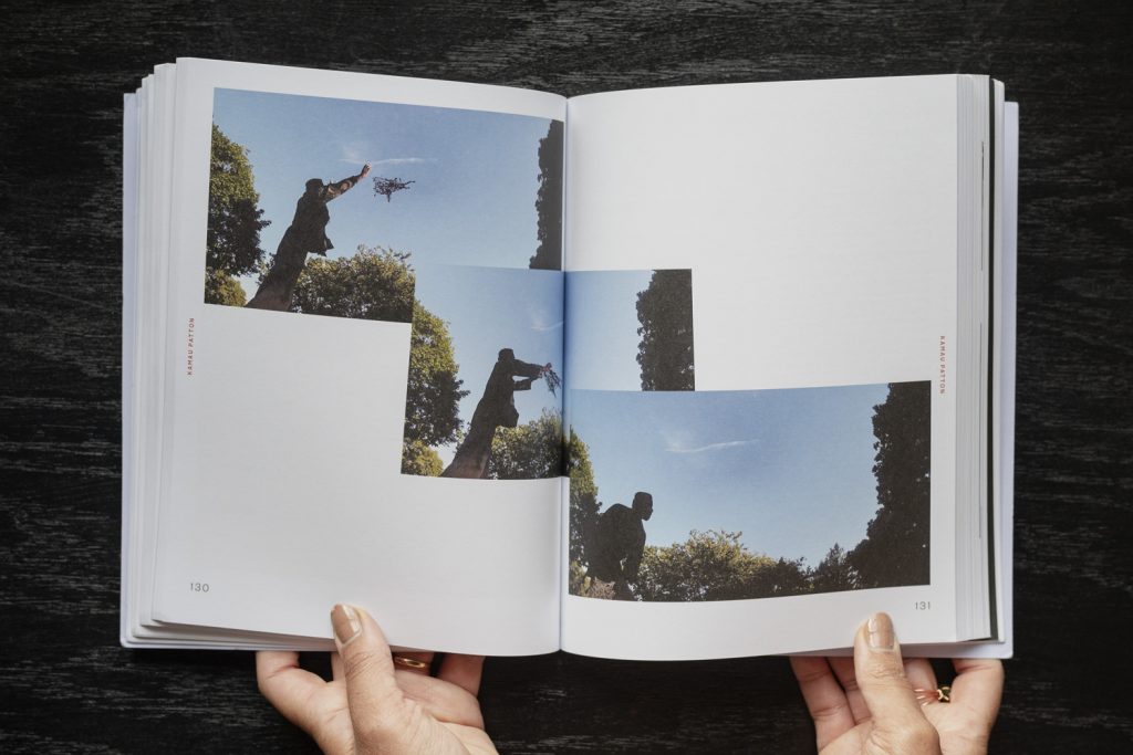 Image: The book Fleeting Monuments for the Wall of Respect is open to pages 130 and 131, showing a series of three photos by Kamau Patton, each photo overlapping. Patton is mid-performance, standing in a tree-filled area on a sunny day with blue skies. The artist is seen from below and silhouetted, in the process of throwing a web of fibers into the sky. Photo by Ryan Edmund Thiel.