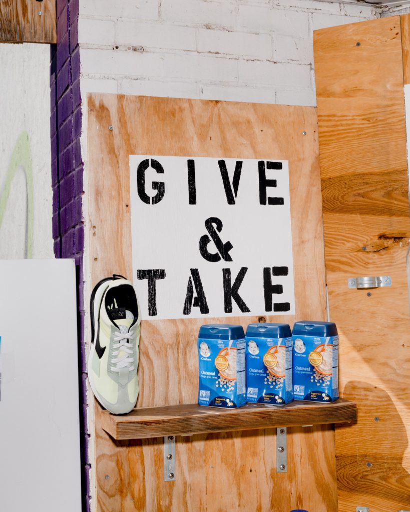 Image: Detail of alt_ market installation, including a sneaker, containers of baby food, and a sign on the installation reads, “ Give & take.”  Photo by Lyndon French. 