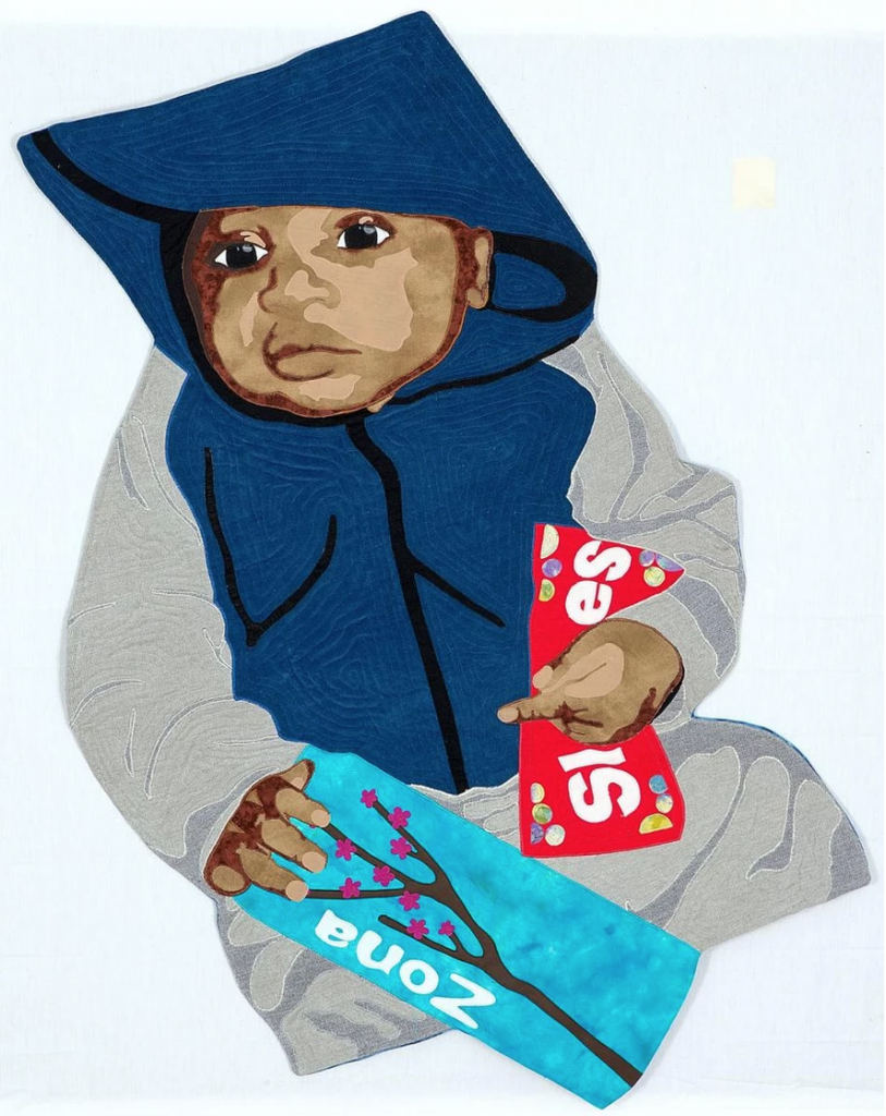 Photo of Dorothy Burge's protest quilt banner dedicated to Trayvon Martin. The image is of an infant child wearing a grey and blue hoodie and grey bottoms. In one hand they are holding a pack of Skittles, in the other hand is a bright teal blue can on Arizona Iced Tea–items that Trayvon Martin bought shortly before his murder. On the quilt you can see the stitching on the surface of the fabric in a labyrinth-like design. Image courtesy of Dorothy Burge.