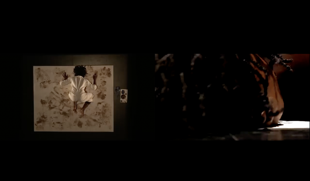Image: A screenshot of Evidence, divided into two frames. The camera on the left is from directly above Akinbola's canvas, showing Akinbola in the center of the canvas, wearing a white suit. The canvas has a a variety of brown markings. The right image is up close on Akinbola's face, with her hair falling in front of her eyes. Her chin is illuminated. Image by Benji Hart.