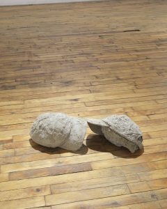 Image: Gary LaPointe Jr., (carhartt hat arch), 2019, Carhartt hats, concrete, 5.5" x 8" x 25". Two grey life-sized hats sit on the gallery floor. They face one another and slightly touch. Images courtesy of Heaven Gallery.