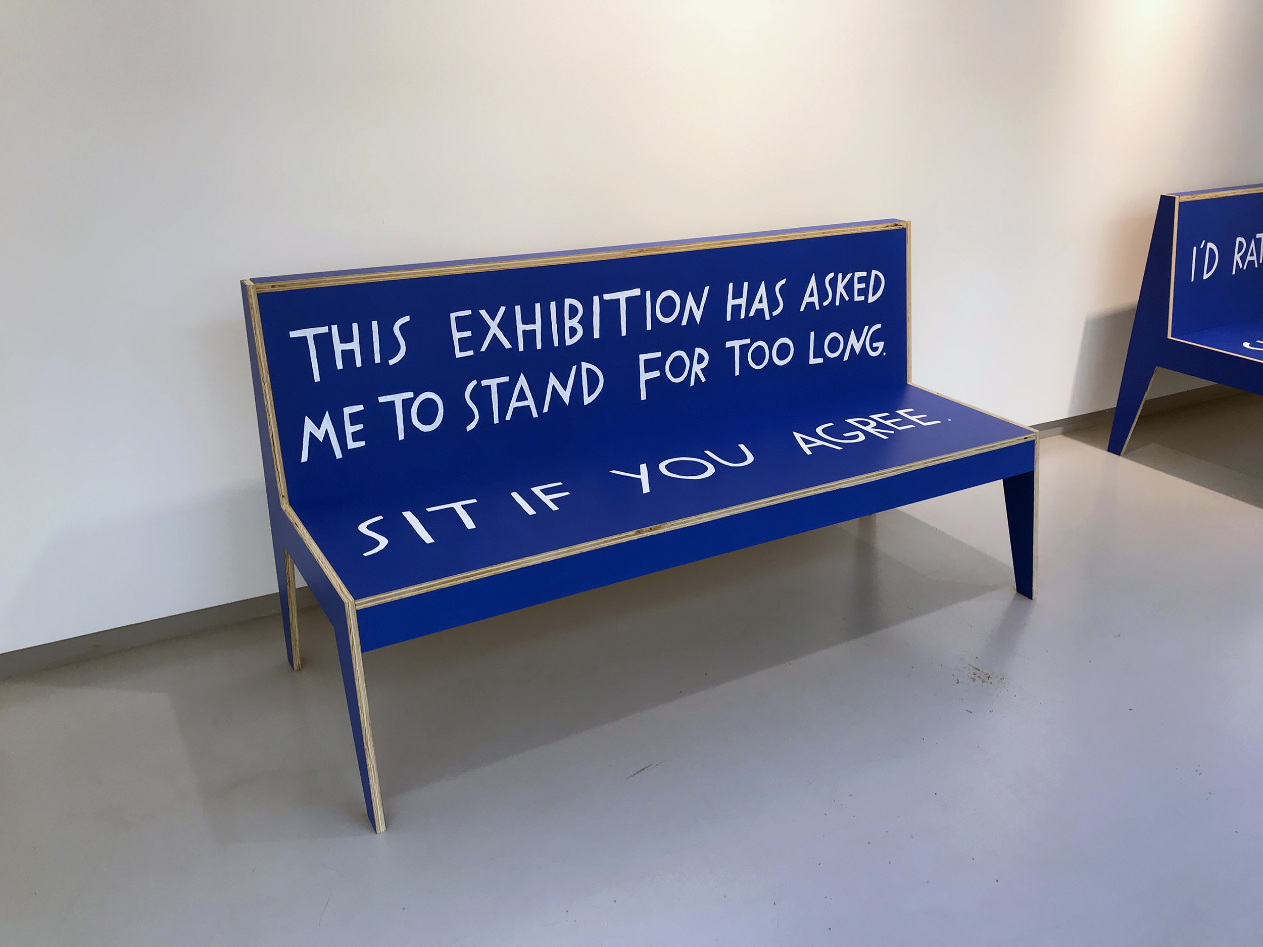 Featured image: Shannon Finnegan, Do you want us here or not?, 2018, MDO, paint. Blue wooden bench in a gallery with text painted on it. The back of the bench reads, "This exhibition has asked me to stand for too long." The seat reads, "Sit if you agree." Image courtesy the artist.