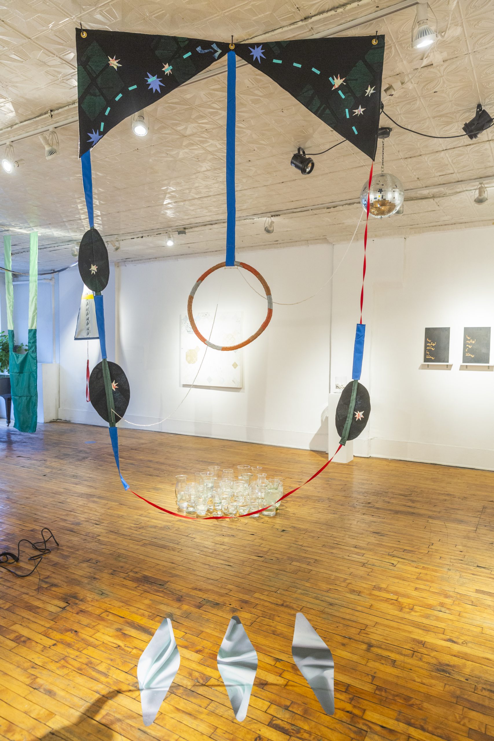Image: "Beckon" (te Ilamo)" by Yesenia Bell, gallery view. There is a circular shape in the center with fabric hanging from the ceiling circling it. The artist has sewn stars into the top, which is a dark grey, black color. In the background is the remainder of the gallery. Photo by Guanyu Xu.