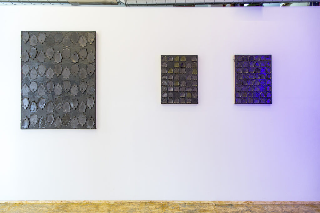 Image: Artwork from left to right: Solar Eulogy by Allen Moore, casted graphite and glue on canvas, 36 x 48"; Red Shift 41 by Allen Moore, casted graphite and glue on canvas, 18 x 24"; Blue Shift 48 by Allen Moore, casted graphite and glue on canvas. A gallery wall with three rectangular black paintings that includes one large rectangular black canvas with 54 cast shapes; one rectangular panel with 41 graphite and glue cast Pac-Man ghosts; one rectangular panel with 48 graphite and glue cast Pac-Man ghosts. Image courtesy of Amy Shelton. 