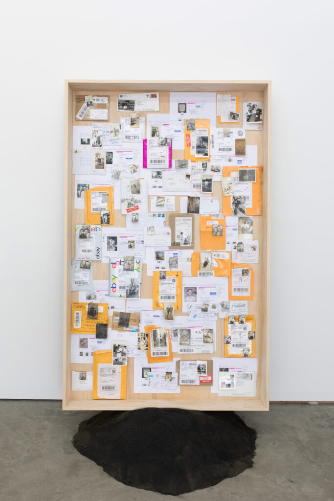 Image: Dear David (Semiotics #2) by Ryan Patrick Krueger. A wooden back and frame seated atop a blobby black pile in a gallery space. Inside the wooden frame are a variety of paper documents, mail packaging, and photos. Image courtesy of the artist and Kalaija Mallery (@goodartdoc).