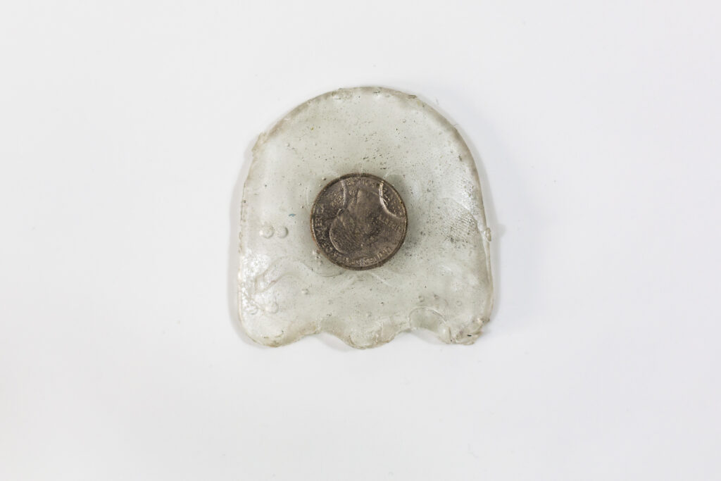 Image: Charon’s Coin by Allen Moore, mixed-media sculpture, approximately 4 x 3" resin-casted Pac-Man ghost with a head-facing quarter in its center. Image courtesy of Amy Shelton. 