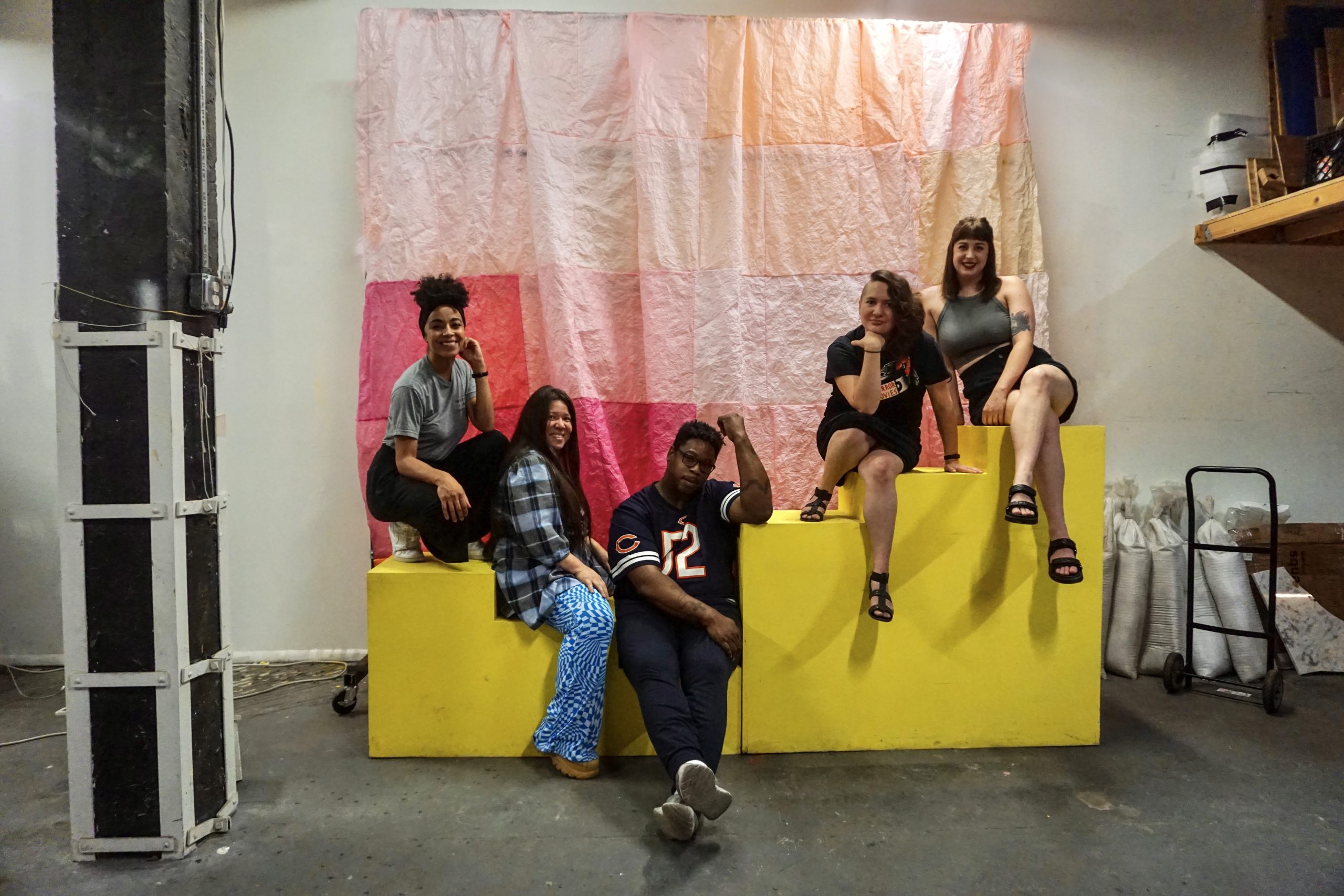 Featured image: A photo of the five Canje cohort members sitting on a yellow platform in front of a pink background at FORTUNA (the studio of Natalia Villanueva Linares). From left to right: Kiki Lechuga-Dupont, Natalia Villanueva Linares, EdVette Jones, Morgan Green, and Christina Nafziger.