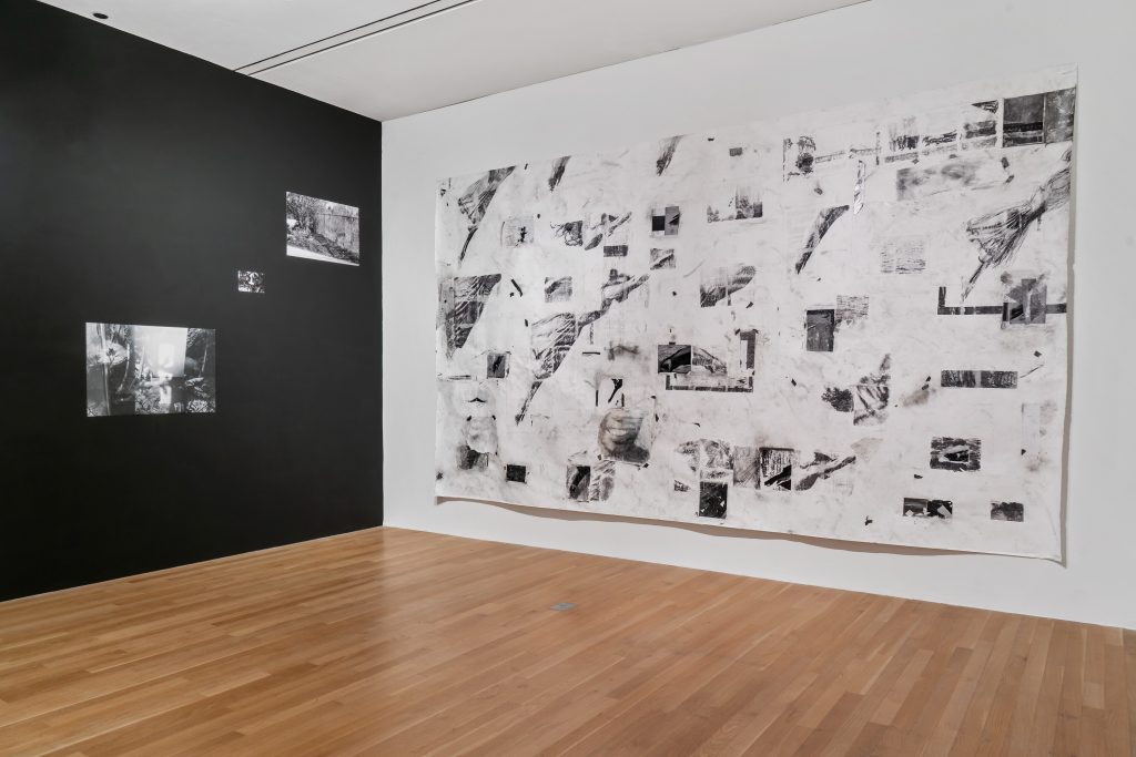 Image: An installation view of Giant Slide by Elissa Osterland (right) and multiple black and white photographs installed on a black wall by Abigail Taubman (left). Photo by Robert Chase Heishman.