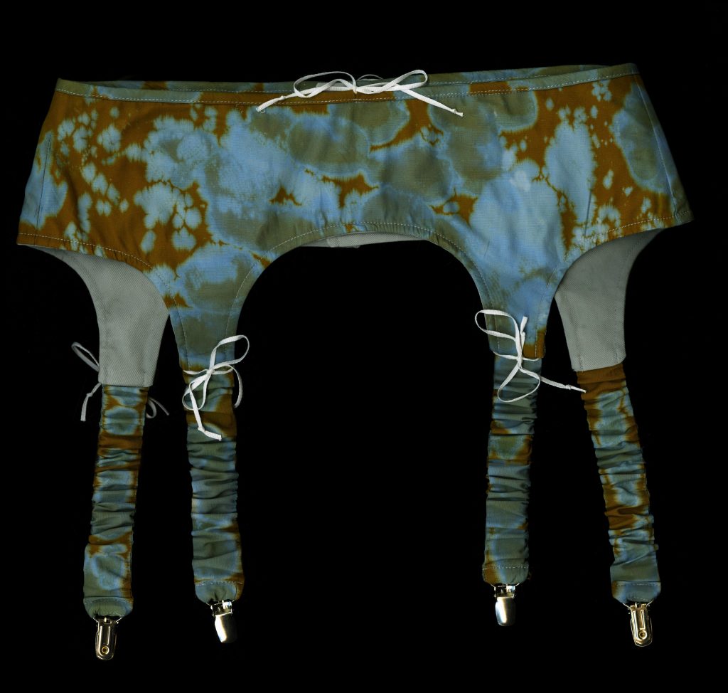 Image: Upside down bra, tie-dyed pungent browns and copper greens, with metal clasps and strings. Photo by Olivia Rehm,