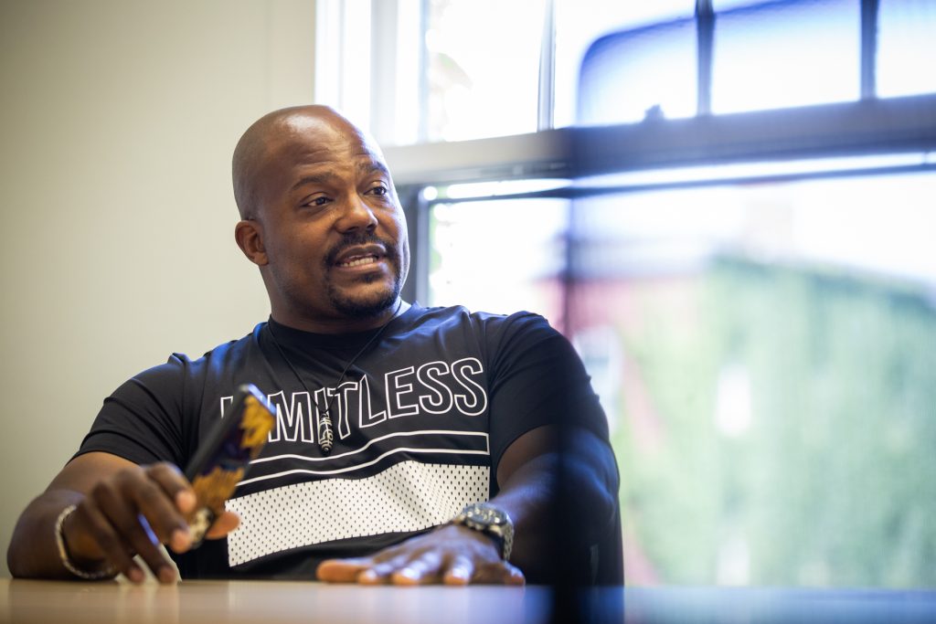 Image: Larry Brent Jr. seated at a table, mid-conversation. His left hand is laid flat on the table and his right hand holds a phone. Photograph by Kristie Kahns.