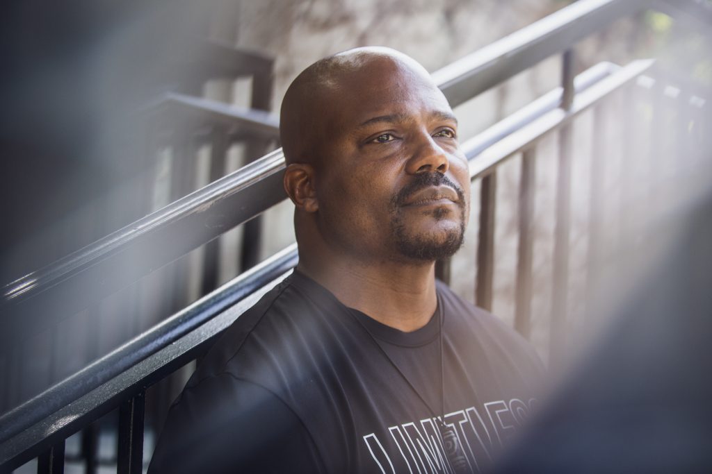 Image: Larry Brent Jr. in front of black handrails, looking up to the left of the photographer. There's a gentle grey distortion on the bottom right and top left hand sides. Photograph by Kristie Kahns.