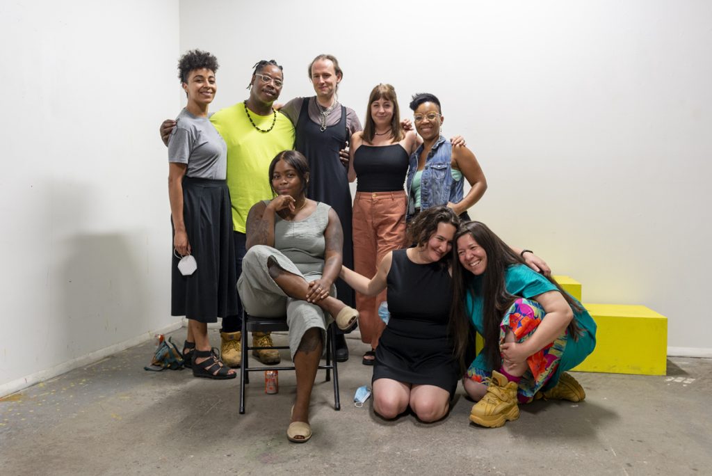 Image: A photo of the second session of CANJE. The following folks stand and sit together while smiling at the camera: Kiki Lechuga-Dupont, EdVette Jones, J Kent, Christina Nafziger, Tempestt Hazel, Rainn Thomas, Morgan Green, and Natalia Villanueva Linares. Photo by Ryan Edmund Thiel.