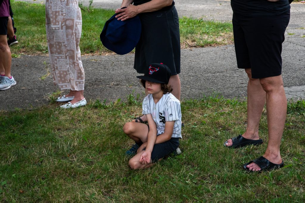 Image: A young boy sits on the grass while people stand around him listening to the tour guide. Photo by EdVetté Wilson Jones.