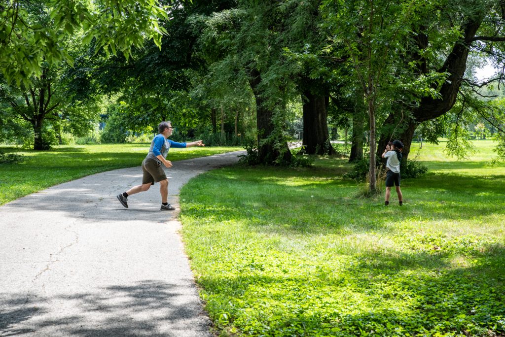 Image: A father and son play a game of stickball with a tree branch and rocks in the park. Photo by EdVetté Wilson Jones.