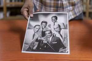 Image: Archivist Dino Robinson holds a black and white photograph of Black folks posing for a photos. The photo is in the collection of Shorefront Legacy Center. Photo by Ryan Edmund Thiel.