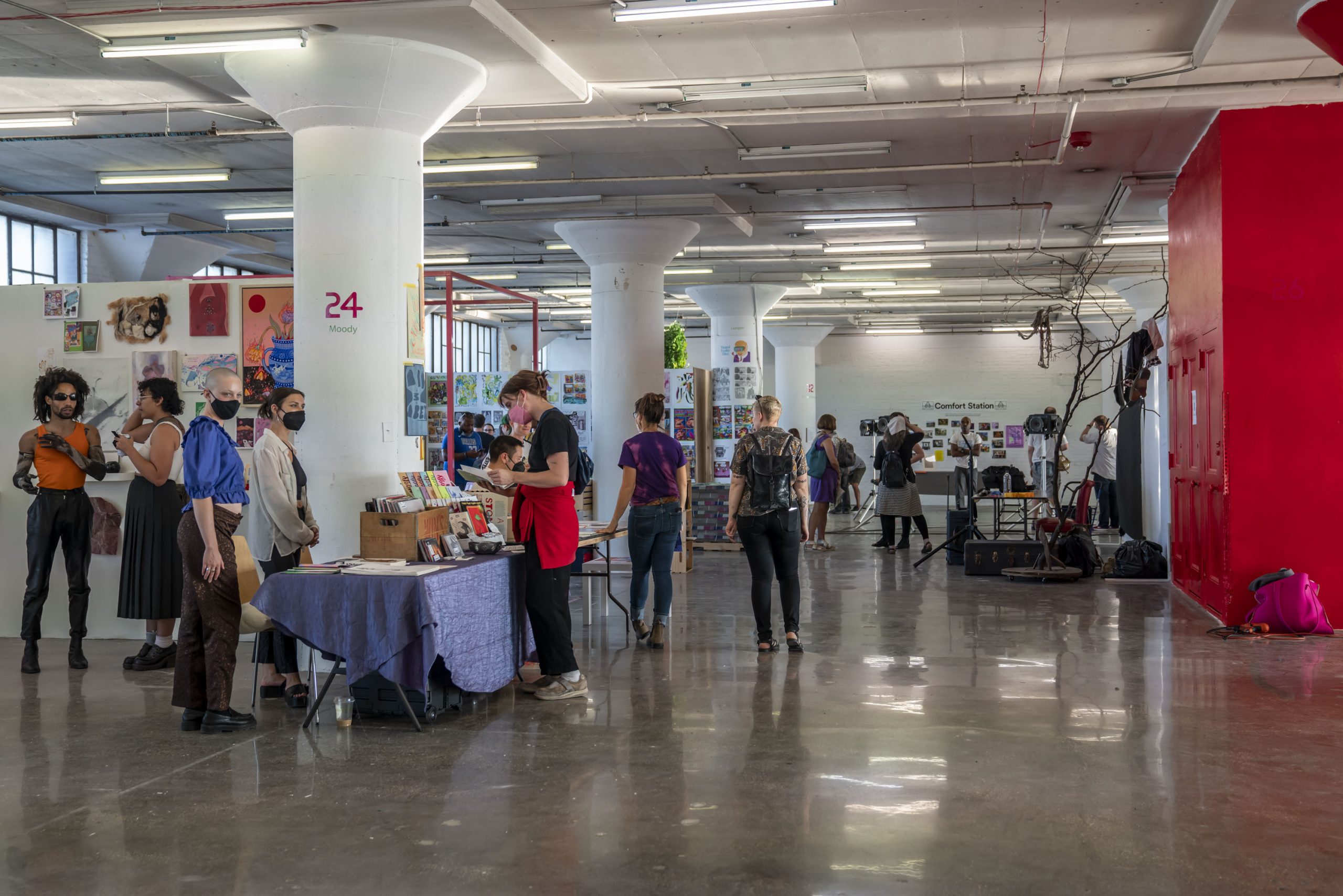 Image: In a high-ceilinged space with beige concrete floors and fluorescent lighting, people attending MdW fair. Photo courtesy of Colectivo Multipolar.