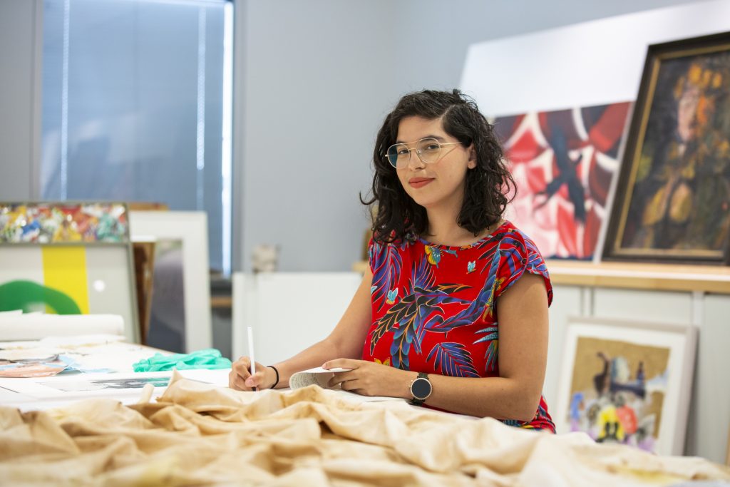 Right Image: Natasha Mijares in the archives of DePaul Art Museum's Latinx collection. She holds a writing utensil as she makes sketches based on the materials around her, which include various art objects from the collection. Photo by Kristie Kahns.