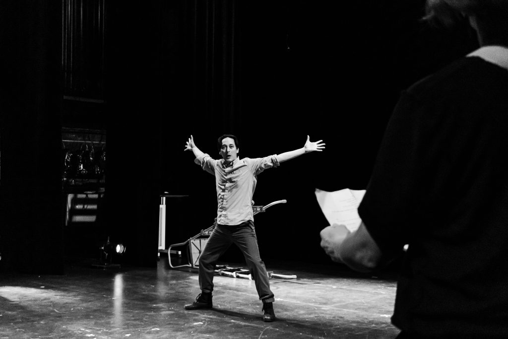 Image: Greyscale photo of Kurt Chiang on a marley dance floor, a ladder laying on the floor behind him. Photograph by Ella Kang.