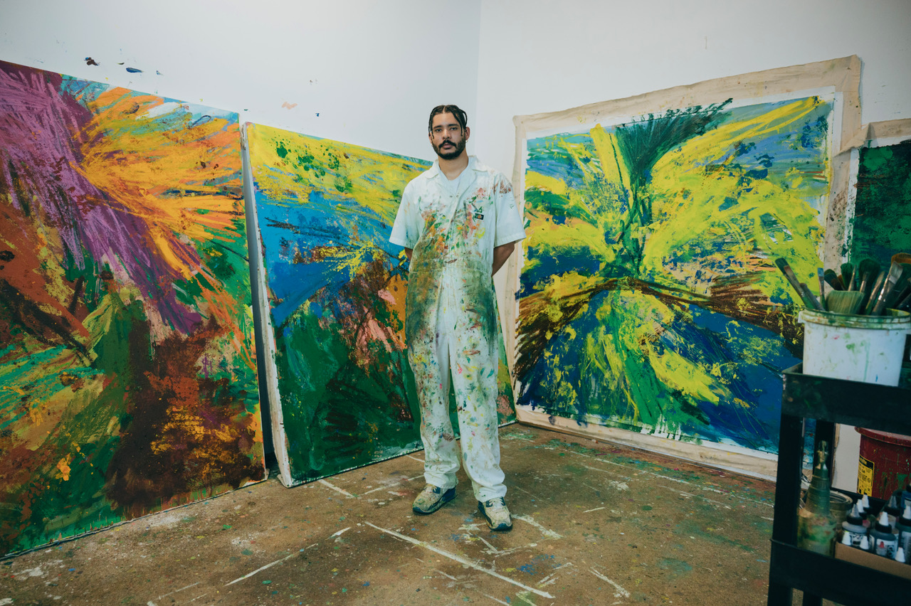 Image: Paul Verdell stands in his studio facing the camera. Behind him are various vibrant, abstract works of his. Photo by Kai Newby. Image courtesy of the artist and Library Street Collective. 