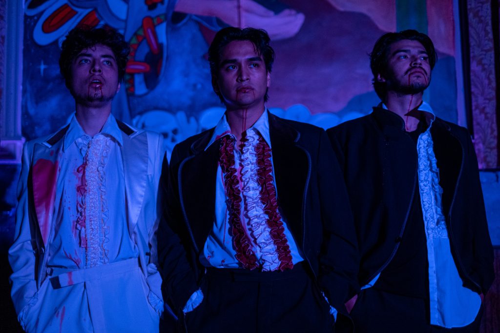 Image: Three actors standing shoulder to shoulder performing a scene in 'The Wizards.' Photo courtesy of the Chicago Latino Theater Alliance.