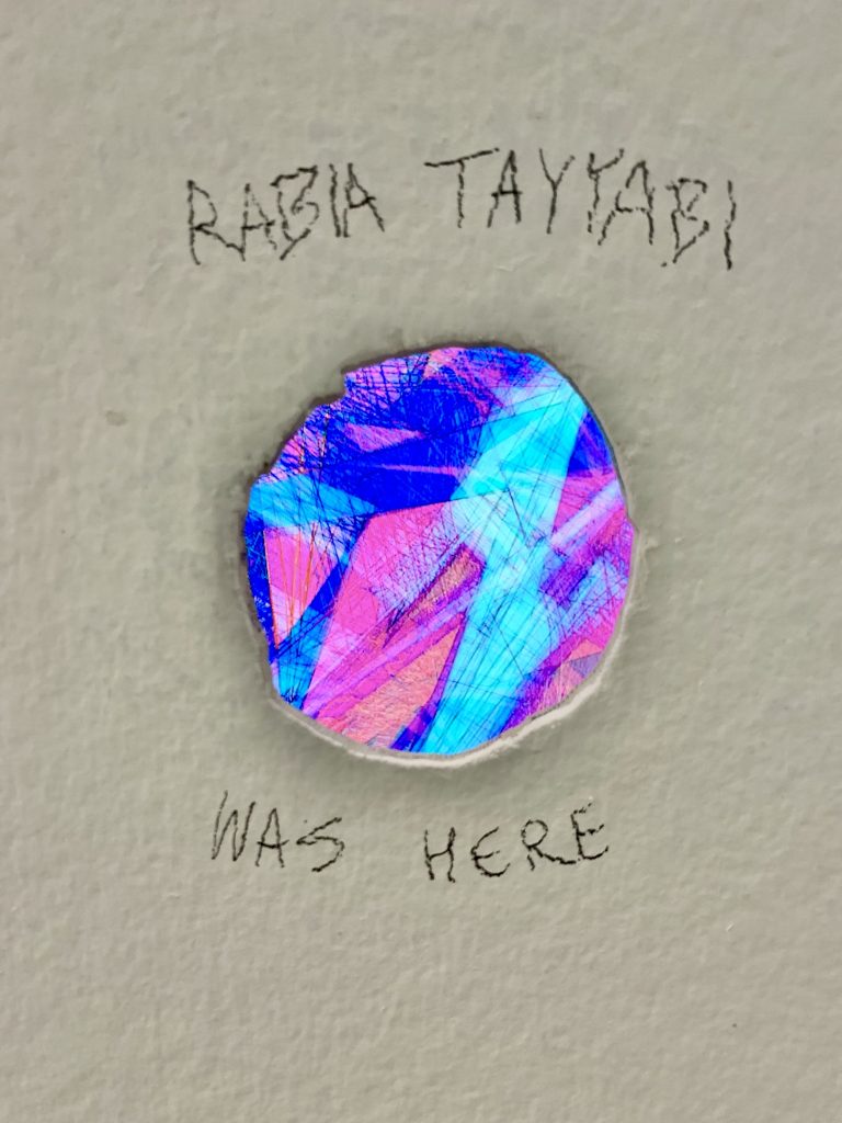 Image: Rabia Tayyabi, Glory Hole, 2022. A hole in a white plaster wall. Written above the hole is "RABIA TAYYABIbia" and written below the hole is "WAS HERE". Visible through the hole is a multicolor abstract coded animation displayed on screen. Images provided by David Downs.