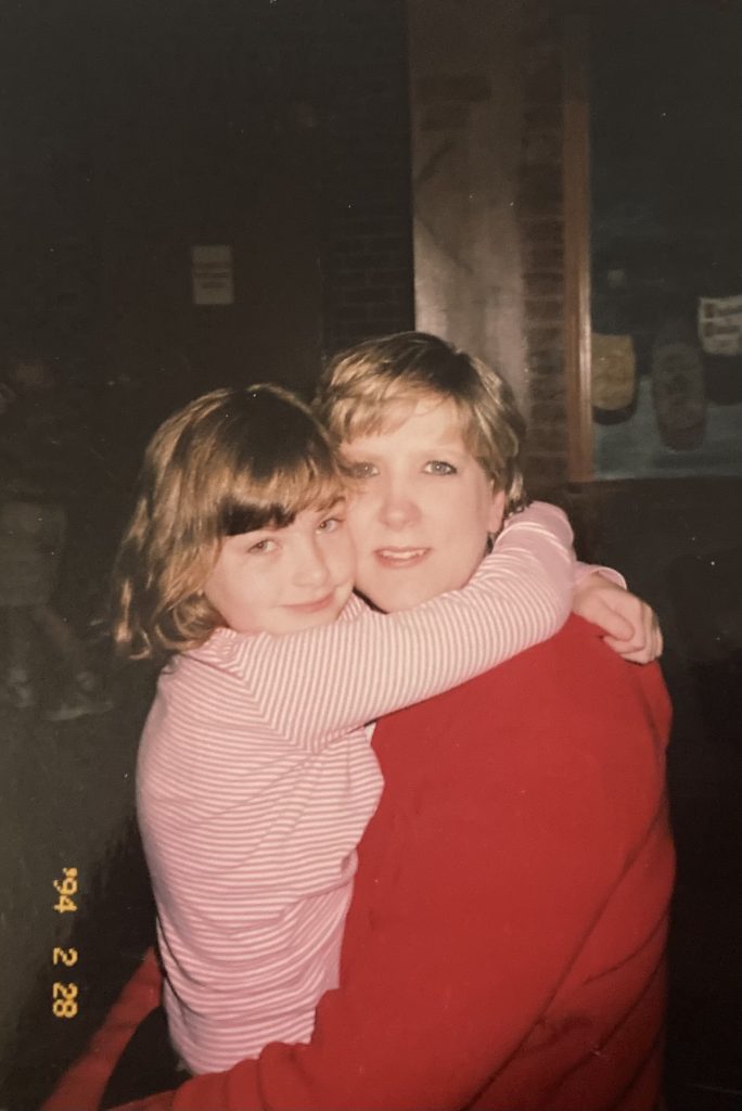 Image: A young woman being tightly embraced by a small child. They both look directly at the camera. Image courtesy of Gabrielle Lynch.