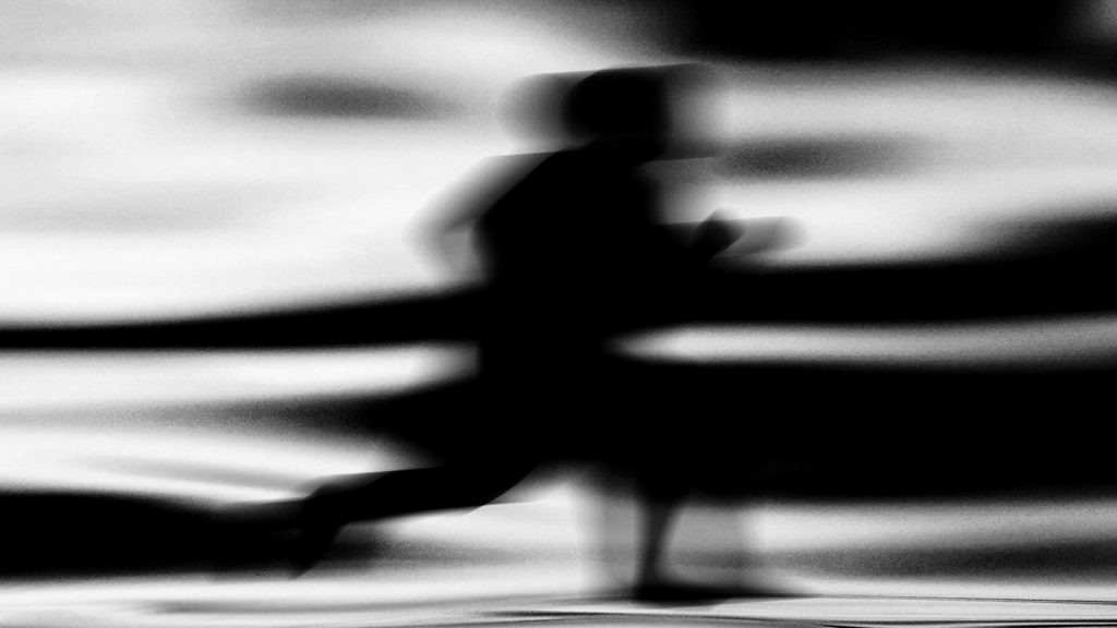 Image: A blurred black figure posed running against a black and white haze. It has no details. Illustration  by Diana C. Pietrzyk.