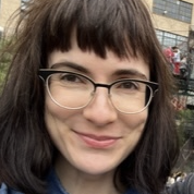 Image: a person with brown bangs and glasses smiles at the camera.