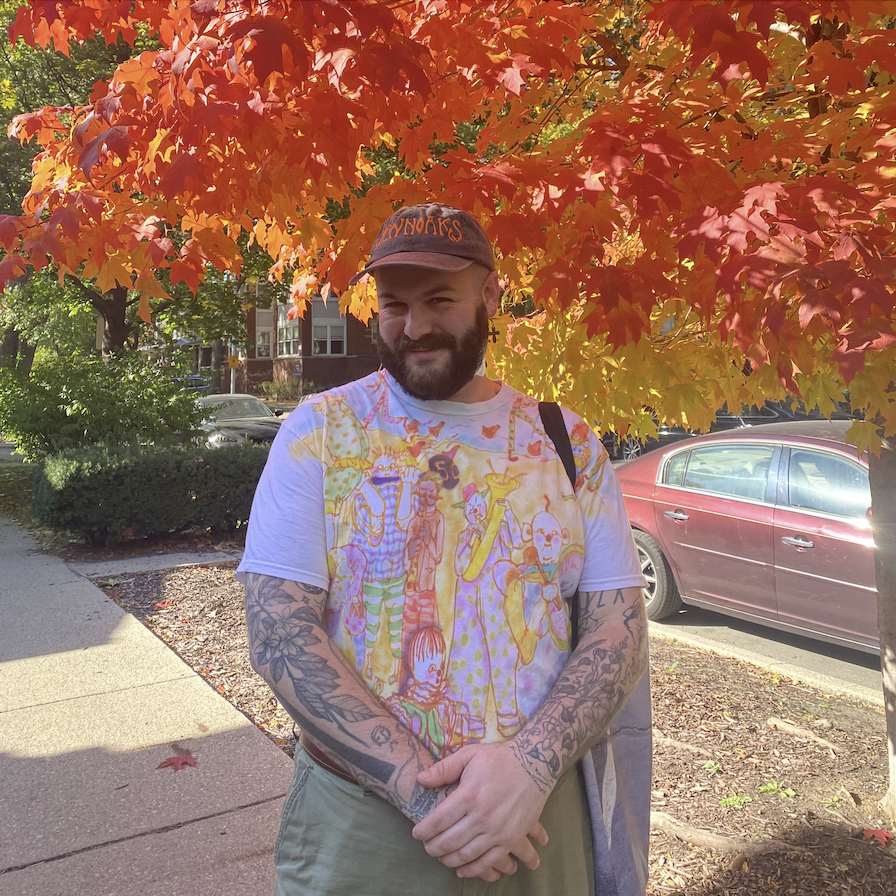 Image: A portrait of Gabriel Chalfin-Piney, who is standing in front of a tree with red autumn leaves while looking at the camera.