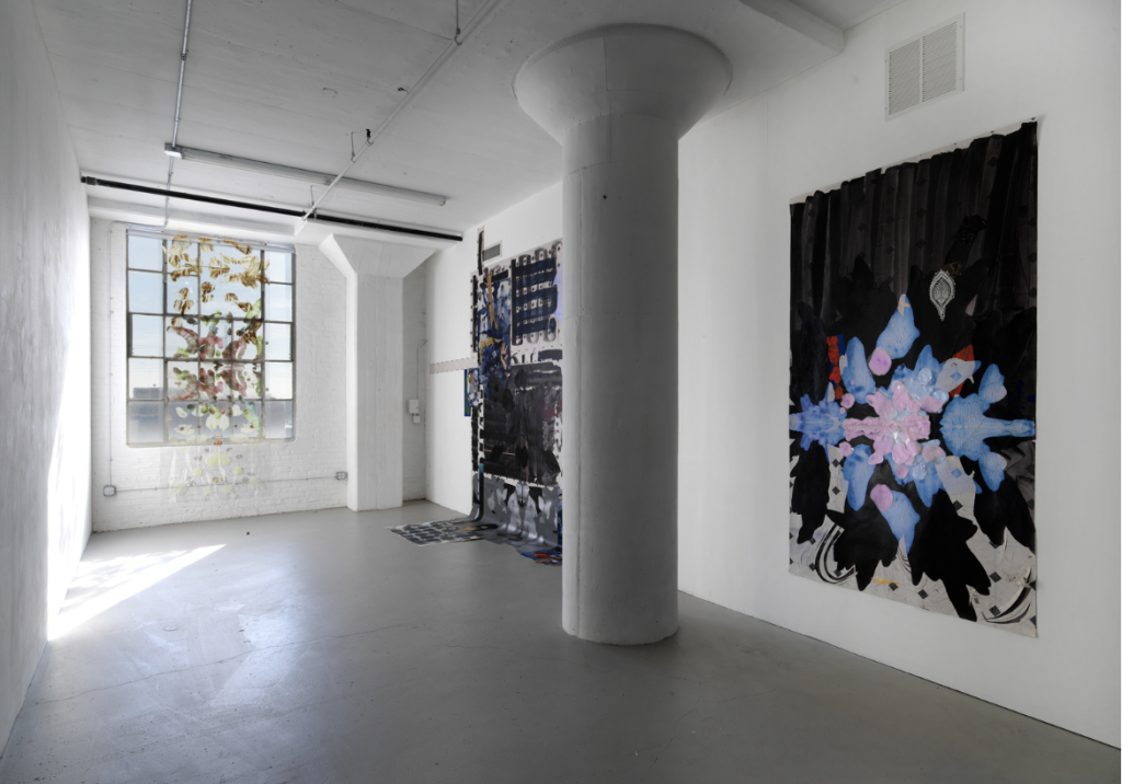 Image: Installation view of LORE at Tiger Strikes Astroid. At the left is a window where there hangs a painting on transparent material. On the adjacent wall, there are two large paintings on vinyl flooring. The one on the left hangs down and onto the floor. Photo by Evan Jenkins.