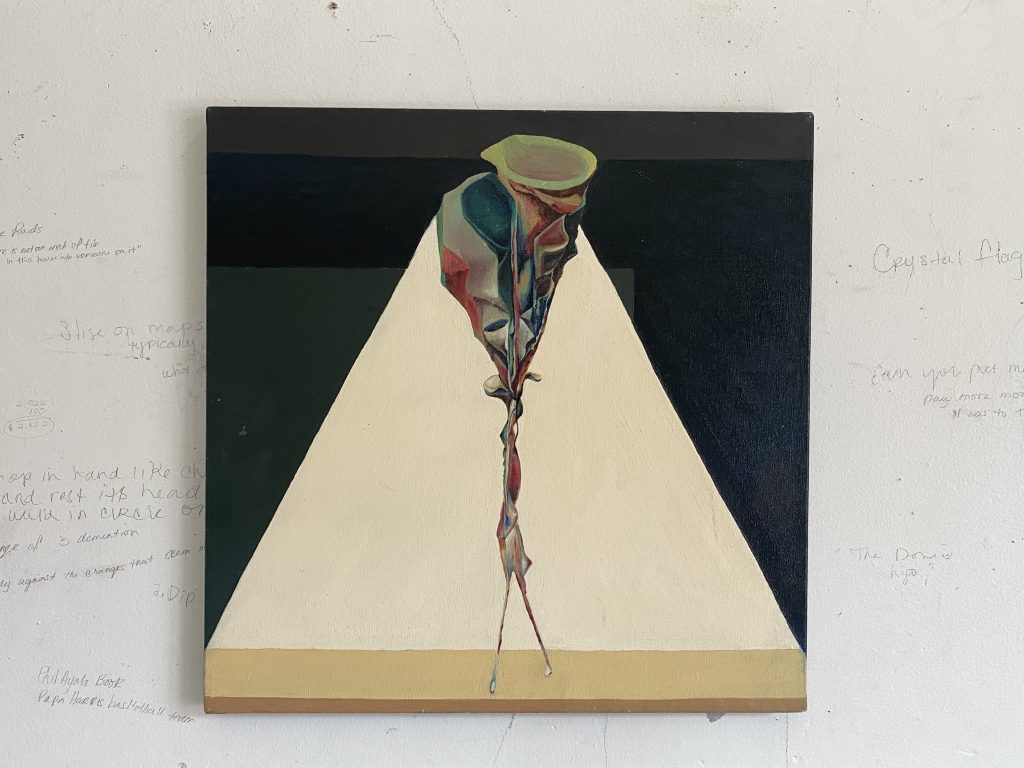 Image: Erol Scott Harris, Taproot, 2014. Oil on linen, 24" x 24". In this snapshot from the studio visit, a painting hangs on a white wall in Erol Scott Harris' studio. On the wall are handwritten notes, writings, and words written in graphite and pen. The painting has a dark green and grey background composed of geometric shapes, with a bright, cream colored triangle surrounding a colorful, abstract, and surreal figure standing at the center. Photo by Tempestt Hazel.