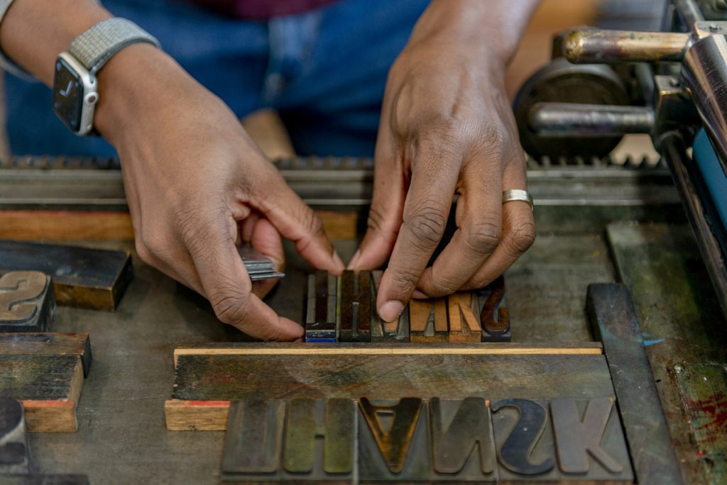Image: Close-up shot of Ben Blount's hands adjusting wooden letters at his letterpress. Photo by Ryan Edmund Thiel.