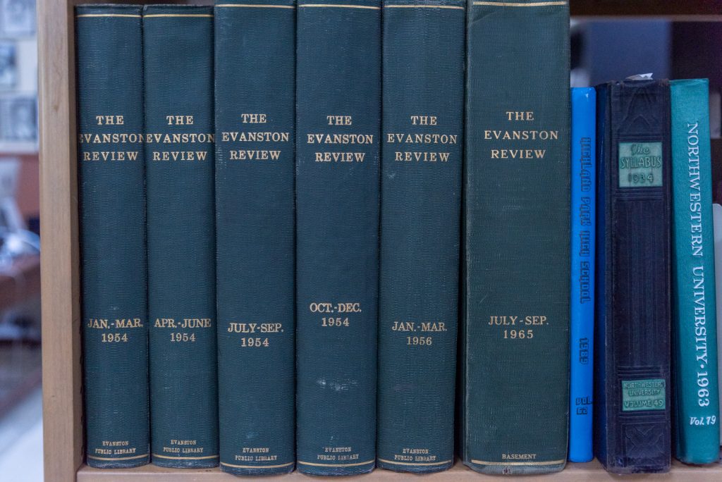 Image: A photo of the inside of the archives at Shorefront Legacy Center, showing a series of dark green books titled "The Evanston Review" through the years 1954, 1956, and 1965. Photo by EdVetté Jones.