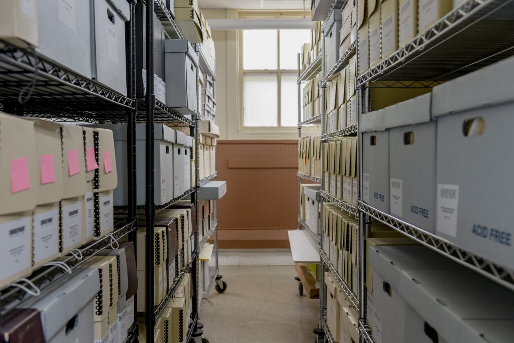 Image: An interior view of the shelves at Shorefront Legacy Center containing shelves of white and cream colored boxes from floor to ceiling. Photo by Ryan Edmund Thiel.