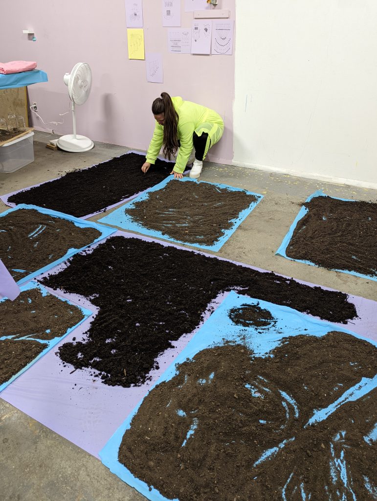 Image: Drying dirt for her installation work, Mina. Natalia Villanueva Linares works on seven blue and purple tarps of soil. Courtesy of the artist.