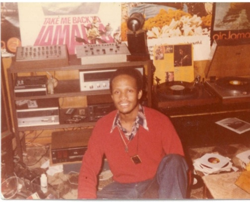 Image: Jerome seated and surrounded by records on vinyl, posters, and other DJ equipment. Courtesy of Alkebuluan and Jerome Merriweather..