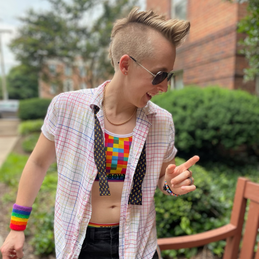 Image: A photo of Brittany Gray wearing a rainbow-colored outfit and sunglasses. She is in mid-motion and is slightly turned to our right.
