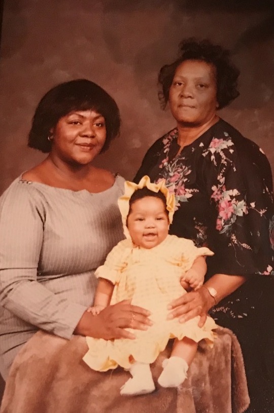 Image: Vanita holds an infant Alexis in her lap. Vanita's mother stands to the side and embraces Alexis. The photo is sepia-toned, though in color. Image courtesy of Green family. 