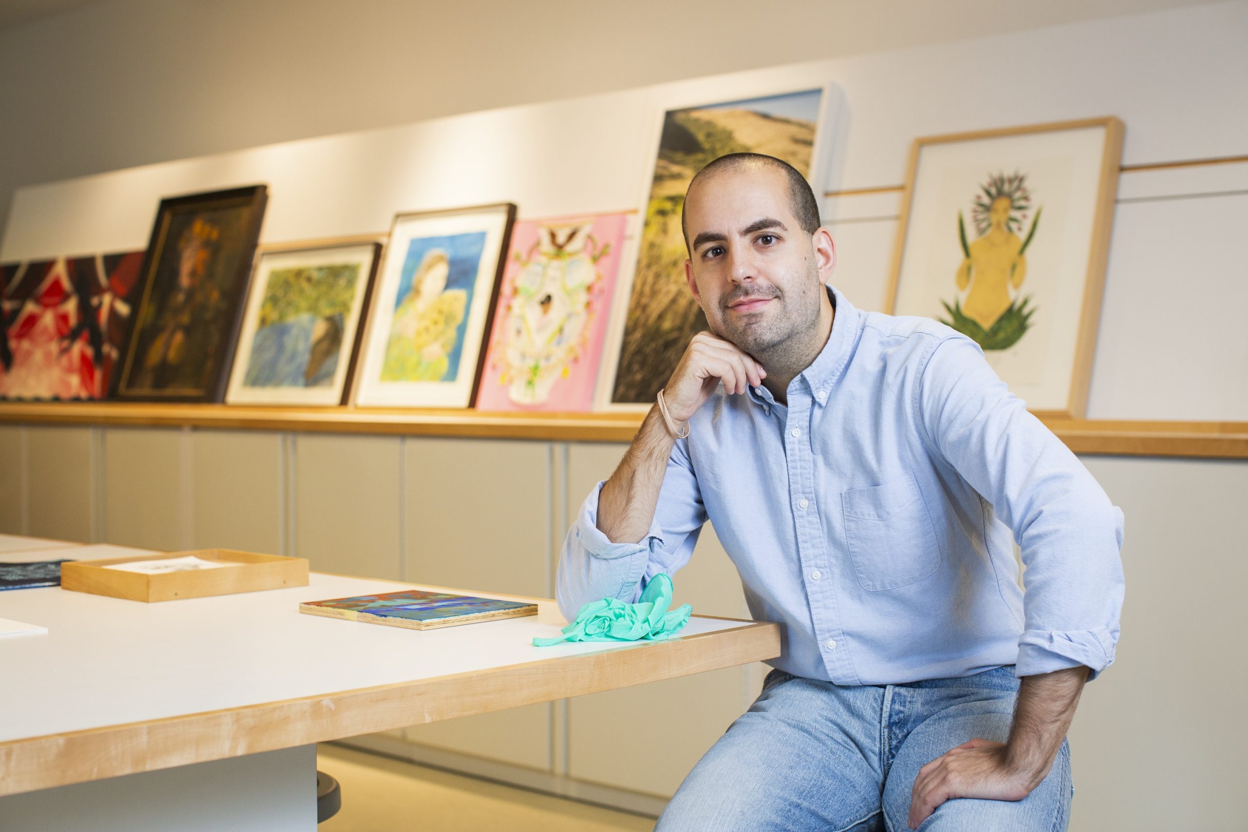 Featured Image: David Maruzzella sits at a table in the DePaul Art Museum Archives. He is wearing a light blue button-up shirt and jeans. Photo by Kristie Kahns.