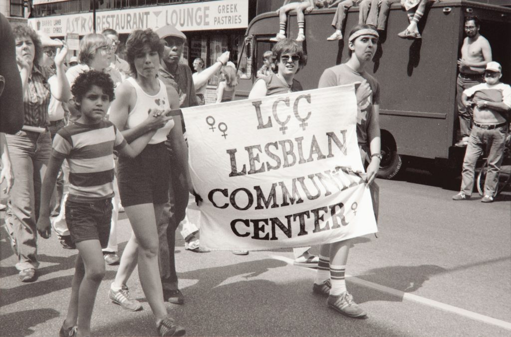 Image: Diana Solís, Mother and Son, 11th Annual Gay and Lesbian Pride Parade Chicago, June 1980, 1980. Photograph of a group of people, including a mother and son, during a parade. Three people carry a sign saying "LCC Lesbian Community Center." Archival Piezography Print. Image courtesy of DePaul Art Museum, Art Acquisition Endowment Fund.