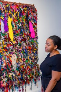 Image: Portrait of Bryana Bibbs and her "Alone Against It All," 2022. Approx. 5.5’ x 5.5.’ Handwoven, hand-carded, hand-spun wool, bamboo fiber, angelina fiber, nylon fiber, and recycled sari silk. Photography by Tonal Simmons.