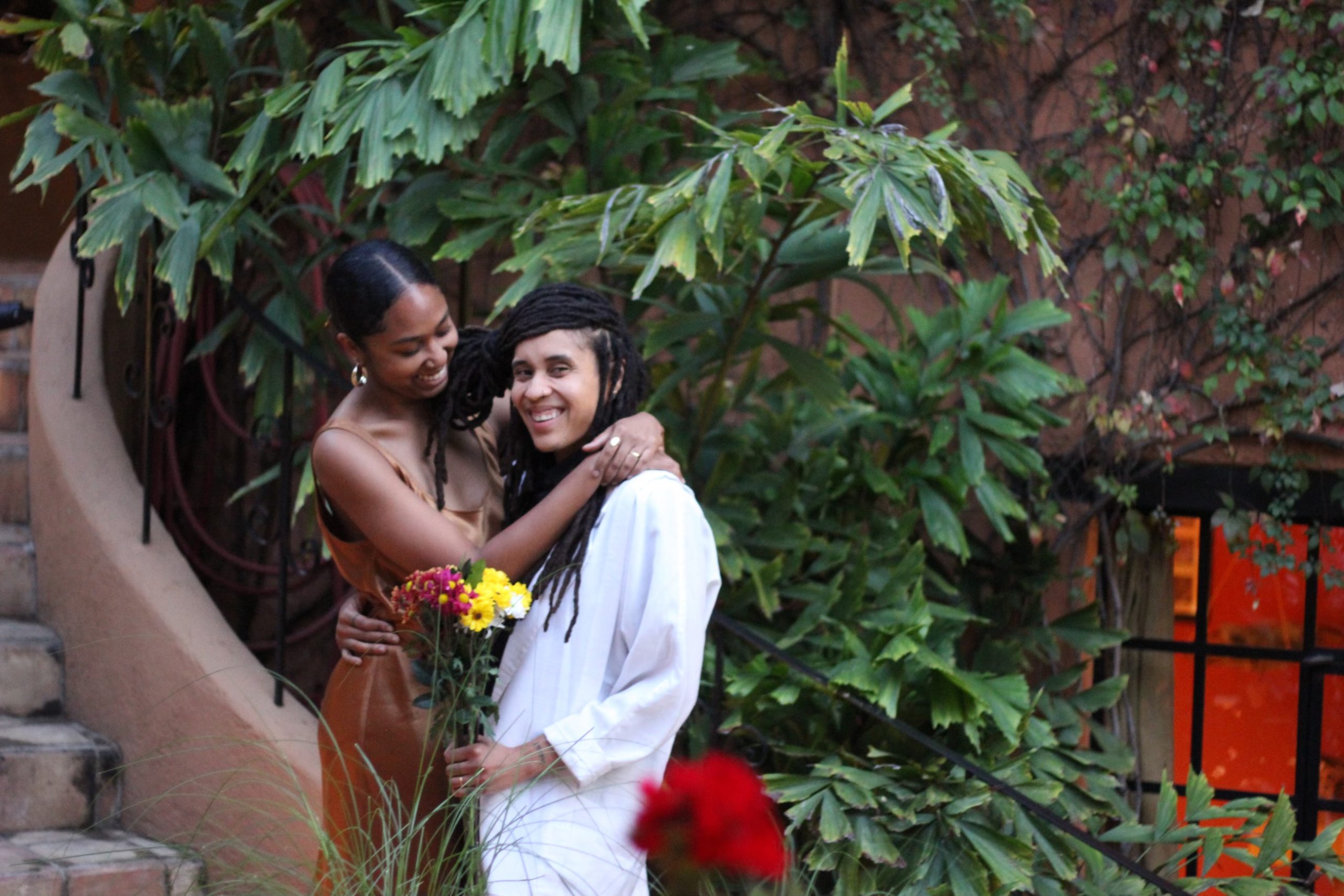 Image: zakkiyyah and Ciera stand together outdoors in front of a large plant and a brownstone. Photo courtesy of the artists.