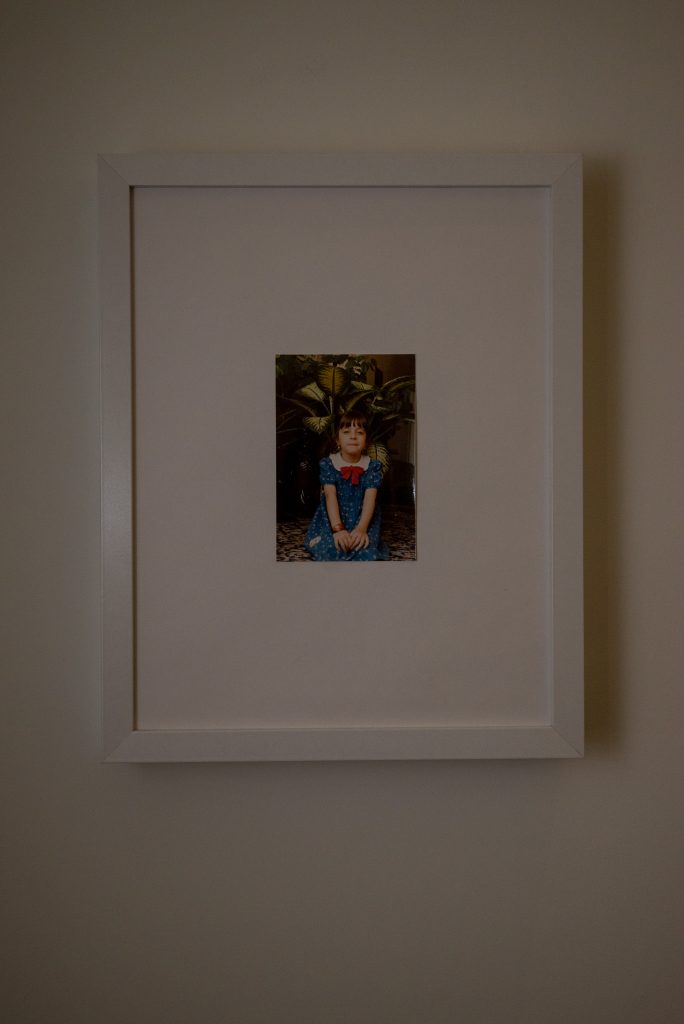 Image: Untitled, Laleh Motlagh. A framed photo of the artist as a child. She wears a blue dress with a red bow on her neck. Image courtesy of the artist.
