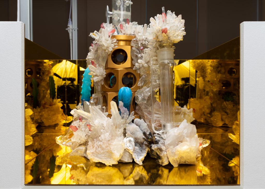 Image: An installation view Soccer Club Club's booth at Barely Fair, featuring the work of Jonah Freeman and Justin Lowe. A gold space with a tower of organic rocks, crystals, tubs, and blocks in the center. Photo by roland miller.
