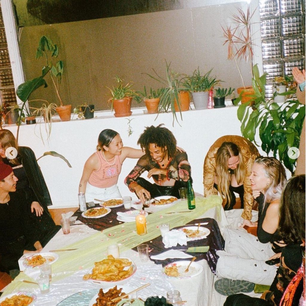 Image: Francine and Antonio sit at the end of a low dinner table surrounded by friends. Francine's arm is wrapped around Antonio as they both are laughing. Photo by Steven Piper.