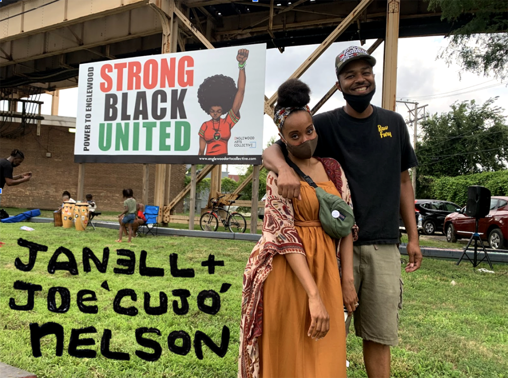 Image: Janell and Joe stand outside in front of a large sign that says "Strong, Black, United." Their names can be seen in the bottom left corner. Photo courtesy of the artists.